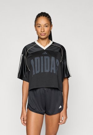 Top scurt negru din plasă cu logo-ul „ADIDAS”; mâneci scurte cu tiv contrastant. Asortat cu pantaloni scurți negri, având un mic detaliu cu logo.