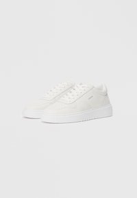 White sneakers made of smooth leather with perforated detailing, round toe, lace-up design, and a thick rubber sole.