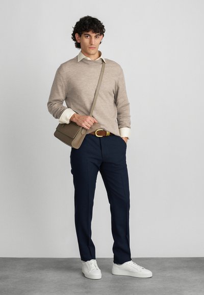 Bežs džemperis, krēmkrāsas krekls, tumši zili bikses, baltas sneakers, brūna josta, pelēka soma. Moderns piegriezums ar gludu tekstūru, minimālistisks dizains.