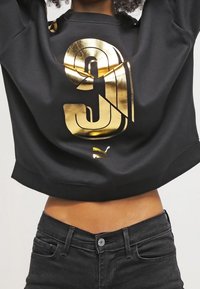 Sweat-shirt noir court avec un grand chiffre "9" doré et un petit logo Puma. Le tissu semble doux avec une texture lisse.