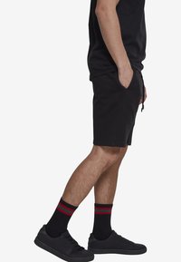 Shorts en coton noirs avec poches latérales et taille élastique, associés à des baskets noires et à des chaussettes noires avec des rayures rouges et vertes.