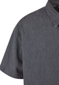 Camicia a maniche corte in tessuto grigio scuro dalla trama leggermente ruvida, dotata di colletto e dettagli di cuciture sottili. Linee pulite e design minimalista.