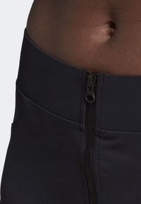 Černé sportovní kalhoty s viditelným zipem vpředu. Vyrobené z elastického materiálu, s hladkou texturou a přiléhavým střihem.