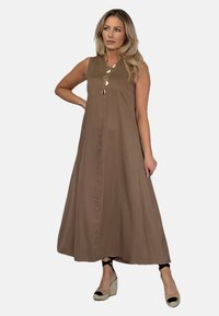 Brązowa bezrękawnikowa sukienka maxi o lekko A-liniowym kroju, z detalem guzików z przodu i lekkiego materiału. Połączona z sandałami na koturnie.