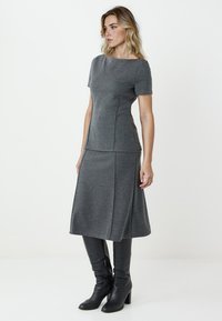 Graues Strickkleid mit kurzen Ärmeln, taillierter Oberpartie und ausgestellt Rock. Kombiniert mit schwarzen Stiefeln bis zum Knie. Glatte Textur, dezentes Design.
