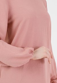 Jasnoróżowa bluzka o teksturowanej strukturze z długimi, bufiastymi rękawami i elastycznymi mankietami, charakteryzująca się luźnym fasonem i delikatnym wzorem marszczeń.