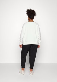 Valkoinen pitkähihaista collegepaitaa, jossa on resorit hihansuissa, yhdistetty mustiin kapeisiin collegehousuihin, nähtynä takaa, valkoisten lenkkarien kanssa.