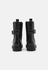 Bottines en cuir noir avec une finition lisse, dotées d'une sangle et d'une boucle, ainsi qu'une semelle en caoutchouc épaisse pour une meilleure traction.