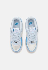 Sapatilhas Nike Air Force 1 azul claro com ponta branca perfurada, detalhes em azul suave e design de atar com acabamentos prateados.