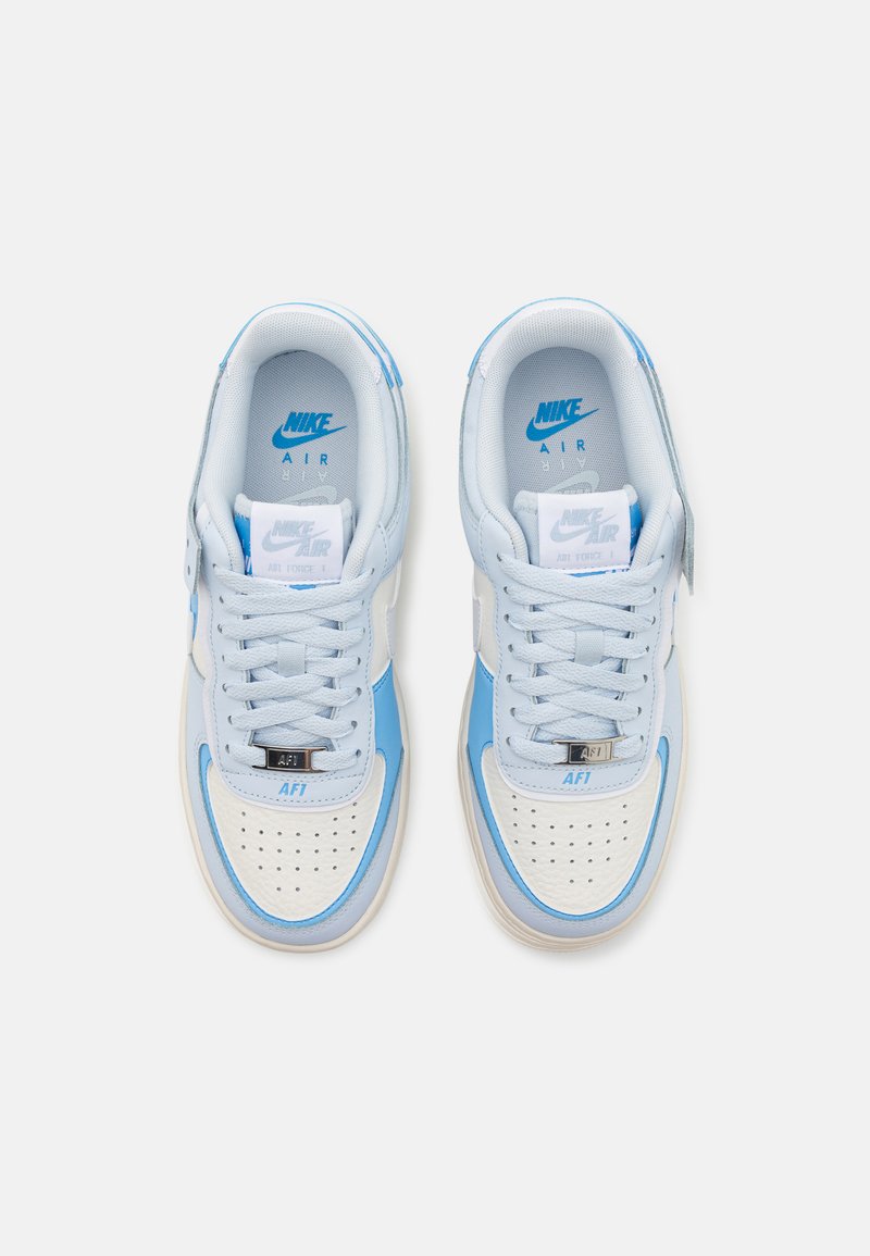 Baskets Nike Air Force 1 bleu clair avec un bout perforé blanc, des accents bleus lisses et un design à lacets avec des éléments en argent.