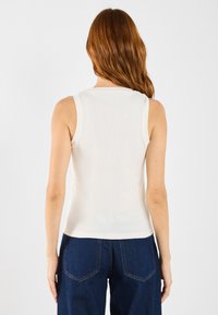 Crème ribbel tanktop met een ronde halslijn, een getailleerde pasvorm en zonder mouwen, gecombineerd met donkerblauwe hooggetailleerde denim broek.