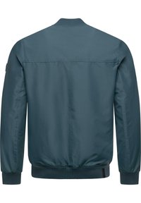 Mėlynas bombonešis su lygiu paviršiumi, raištinėmis rankovėmis ir apatiniu kraštu bei klasikiniu apykakle. Pasižymi minimalistiniu dizainu ir matomo apdirbimo trūkumu.