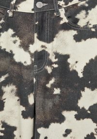 Jeans di denim con motivo a stampa mucca bianca e nera, chiusura con bottone argento e cuciture visibili sulle tasche anteriori.