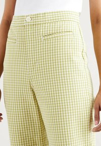 Pantalon à carreaux vichy verts et blancs avec fermeture par boutons, poches latérales et coupe ajustée, fabriqué en tissu mélange de coton.