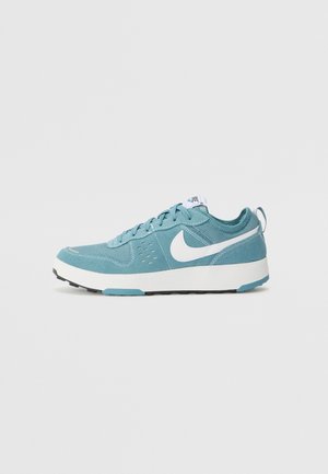 Baskets Nike bleu sarcelle et blanc avec design à lacets, logo Swoosh blanc, semelle blanche épaisse et languette à l’arrière, sur fond uni.
