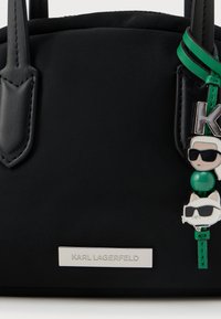 Μαύρη νάιλον τσάντα χειρός με δερμάτινες λεπτομέρειες, διακοσμημένη με μια ασημένια πινακίδα λογότυπου και ένα πολύχρωμο γούρι που απεικονίζει φιγούρες με γυαλιά ηλίου.