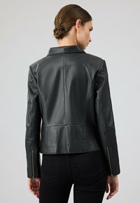 Giacca di pelle nera con un design attillato, caratterizzata da un colletto a intaglio e polsini con zip. Texture liscia, cuciture visibili e dettagli sul pannello posteriore.