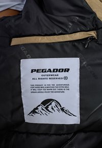 Schwarzer Außenstoff mit einem sandfarbenen Akzent, versehen mit einem weißen Etikett, das Text und eine Berggrafik zeigt, um klare Markenidentität und Details zu gewährleisten.