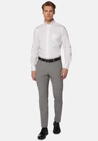 Bela srajca z gumbom in žepom na prsih, v kombinaciji z sivimi teksturiranimi hlačami in črnimi oblekami, z črnim pasom za kontrast.