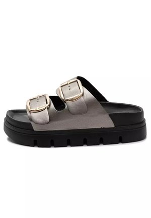 Sandał typu slide z otwartymi palcami, z dwoma szerokimi srebrnymi paskami posiadającymi regulowane kwadratowe złote klamry oraz grubą czarną podeszwą z głębokimi rowkami.