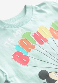 Ljust blått bomulls-t-shirt med ribbad rundhals, prydd med färgglada ballonggrafik och texten "DET ÄR MIN FÖDELSEDAG" ovanför en karaktär.