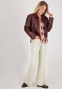 Bordeaux leren jas met een eenvoudige kraag, gecombineerd met een gebloemd topje en lichtgekleurde flared broeken. Bruine schoenen maken de outfit compleet.