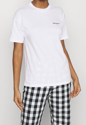 Person trägt ein schlichtes weißes Carhartt T-Shirt und schwarz-weiß karierte Hosen, steht mit entspannten Armen an den Seiten.