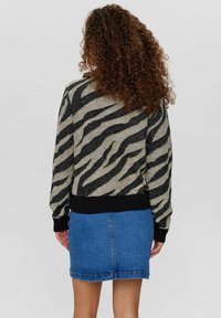 Pulover z vzorcem zebre v bež in črni pletenini, z rebrastimi manšetami in obrobo, v kombinaciji z modrim jeans krilom. Teksturen, sproščen dizajn.