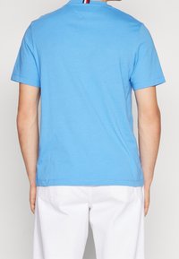 Blå bomullströja med korta ärmar, som har en rund halsringning och ett randigt accent vid nackområdet. Slät textur, avslappnad passform.