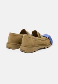 Braune Wildleder-Slipper mit einem kontrastierenden blauen Gummiakzent an der Zehenpartie, ausgestattet mit einer dicken, strukturierten hellbraunen Laufsohle und subtilen Nähdetails.