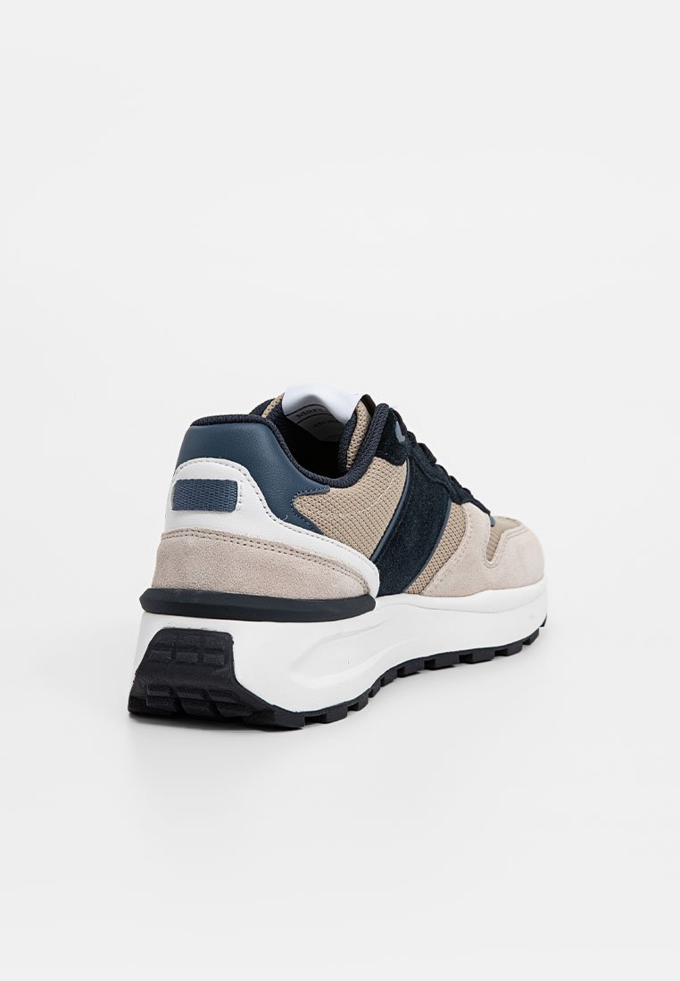 Sneakers met een beige en marineblauwe kleurenschema, gemaakt van suede en textiel, met een dikke witte zool en een gestructureerde zwarte buitenzool.
