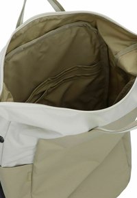 Beige Tote Bag Innenseite mit glatter Textur, ausgestattet mit mehreren Fächern und Taschen, Reißverschluss und einer stoffähnlichen Oberfläche.