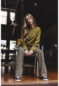 Olijfgroen gebreide trui met een gegolfde halslijn, gecombineerd met gestreepte zwart-witte wijde broek en zwarte sneakers.