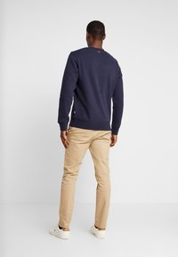 Felpa navy con maniche lunghe e polsini a coste, abbinata a pantaloni beige e sneaker bianche. Design semplice con scollo rotondo.