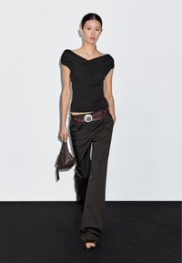 Sort off-shoulder top, løstsiddende sorte bukser, brun bælte med sølvaccent og mørk handbag. Simpelt design og neutrale farver.