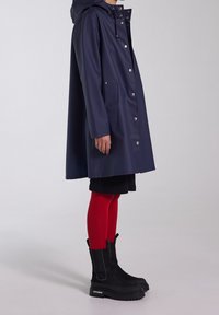 Tmavě modrý plášť s kapucí, zapínaný na knoflíky, s bočními kapsami. Nošený přes černou sukni a červené punčocháče, doplněný černými botami na platformě.