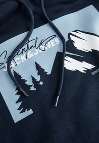 Sudadera azul y oscura con capucha que presenta un gráfico de árboles, el texto "Essentials JACK&JONES" y cordones texturizados con puntas metálicas.