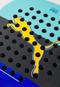 Logo PUMA inciso su una superficie di gomma nera, turchese e blu testurizzata con molte perforazioni circolari, che mostra dettagli arancioni vivaci.