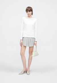 Hvit langermet topp, grå plisséskjørt i minilengde, lysegrå slingbacks, liten kremfarget håndveske. Enkel, moderne og minimalistisk design.