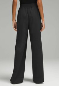 Zwarte, wijde broek met een getextureerde elastische tailleband. Glad stof valt zacht van de taille tot de zoom, met een nette afwerking aan de boorden.