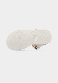 Λευκή σόλα παπουτσιού με υφή λουλουδιών και πεταλούδων. Διαθέτει λεία επιφάνεια και ετικέτα εμπορικού σήματος κοντά στη φτέρνα.