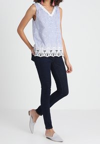 Top sin mangas de color azul claro con escote en V y ribete de encaje blanco. Combinado con jeans skinny oscuros y zapatillas grises sin cordones.
