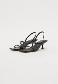 Sandali con tacco in pelle nera caratterizzati da strisce sottili, punta quadrata e tacco sottile. La superficie è liscia con dettagli di design minimalisti.