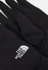 Black gloves made of stretch fabric, featuring textured grip patches on the palms and a white logo on the wrist area.