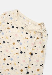 Beżowa koszula z długim rękawem, ozdobiona kwiatowym wzorem w odcieniach niebieskiego, różowego, żółtego i czarnego. Miękka tkanina z zaokrąglonym dekoltem i zatrzaskami.