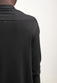 Černý pletený svetr s jemnou texturou. Má kulatý výstřih a malý dekorativní prvek na zadní straně. Minimalistický design.