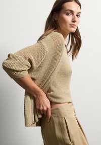 Maglione a maglia di un beige chiaro, con una vestibilità rilassata, motivi testurizzati e maniche ampie. Abbinato a pantaloni beige chiaro.