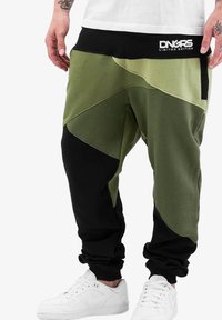 Pantaloni de trening verzi și negri cu un design geometric, realizați dintr-un material din amestec de bumbac. Au o talie elastică cu marcă și buzunare laterale.