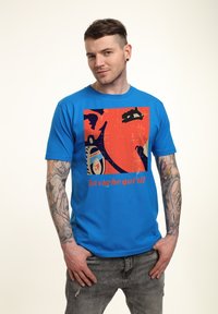 Blå bomullströja med en grafisk tryck i orange och svart, med texten "la vache qui rit" synlig längst ner.