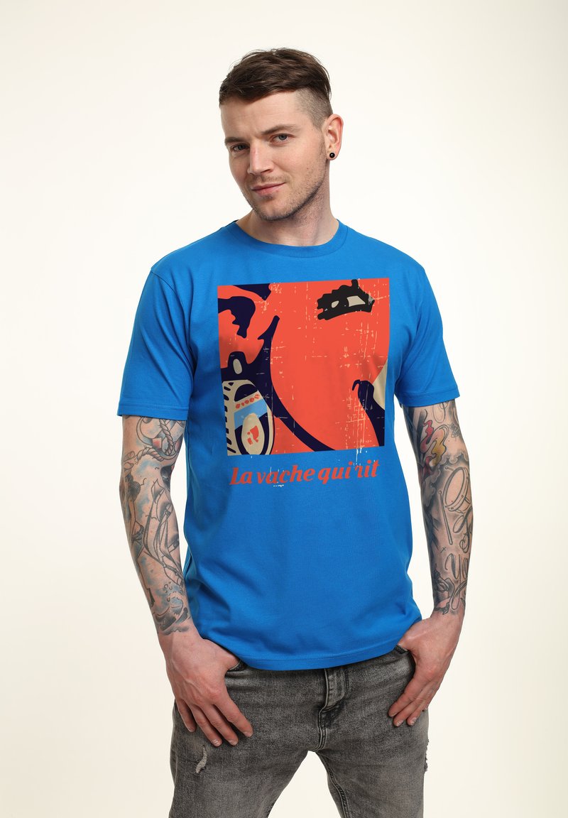 Blå bomullströja med en grafisk tryck i orange och svart, med texten "la vache qui rit" synlig längst ner.